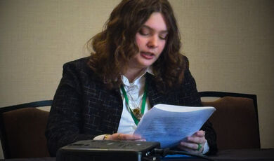 A woman sits and reads from a piece of paper 