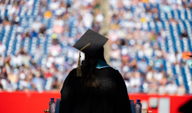 Student stands on commencement stage looking out to the crowd 