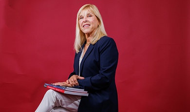 Dr. Lisa Battaglino sits on a stool holding books in front of a red backdrop.