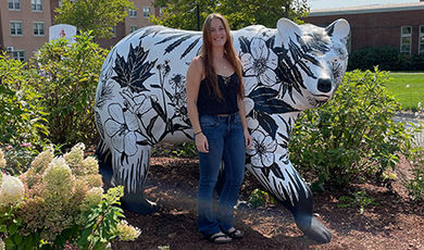 Sam Cushman stands in front of the bear statue she painted with images of native plants.