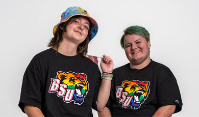 Two students standing wearing black tshirts with rainbow bears on the front 