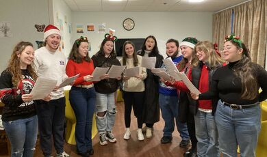 A group of people hold a sheet of music and sing together