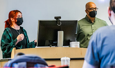 Carrie Provost stands next to a computer giving a presentation to students.