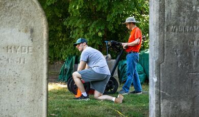 Framed by two gravestones, a professor and student work with ground-penetrating radar.