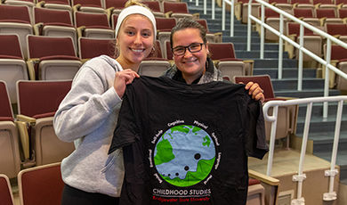Two students hold a childhood studies t-shirt showing a globe.