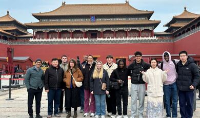 A large group of students stands next to a building in the Forbidden City.