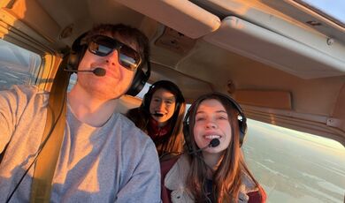 Three people fly in a small plane while wearing headsets.