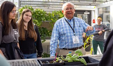 A professor and students gather around a cucumber plant in a greenhouse.
