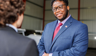 A man wearing glasses smiles as he listens to another man talk 