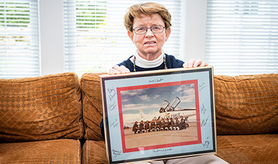 Mary Donahue sits on a couch holding a photo of her and her fellow Air Force pilots