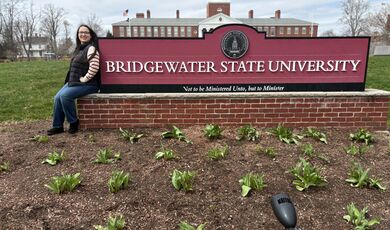 A woman leans on a Bridgewater State University sign