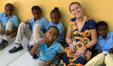 Ellie Roberts smiles sitting on the ground with some of her students 