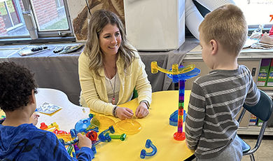 Melissa Schwalbe works with two young students at a table in her school.