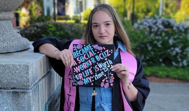 A woman stands holding her graduation cap 