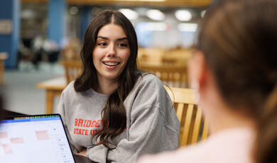 A woman with long brown hair smiles while talking to another woman