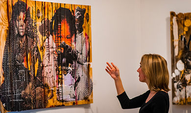 Elizabeth Ezekiel points at a fence panel covered in a collage in the art gallery.