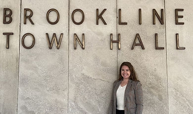 Devon Fields stands in front of a sign saying "Brookline Town Hall"