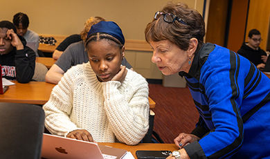 Evie Dewar works with a first-generation student on a laptop.