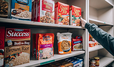 A student grabs a box of food off a pantry shelf.