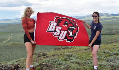 Olivia and Julia hold a red flag with the BSU bear logo in the Montana mountains.