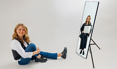 A photo with a white background showing Mackenzie sitting on the ground and in a mirror dressed in a graduation cap