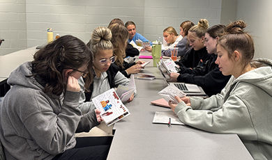 Students sit at a long table reading and discussing zines.