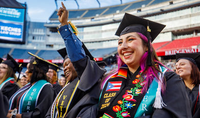 A graduate smiles while another points triumphantly at the sky