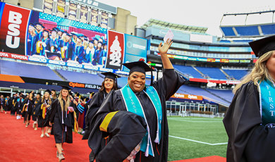 A graduate waves to the crowd while walking to her seat.