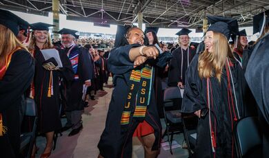 A graduate dances in the aisle as others cheer her on enthusiastically.
