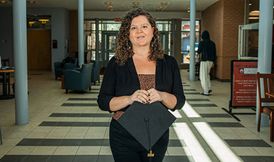 Jamie Jackson stands in the ECC lobby while holding a graduation cap.