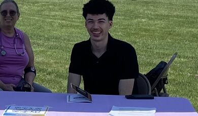 A young man sits at a table and smiles 