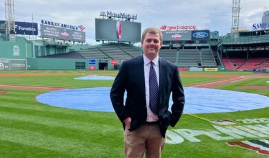 A man stands wearing a suit at a baseball park 