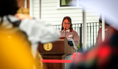 Joanne Tanaka stands behind podium and delivers a speech 