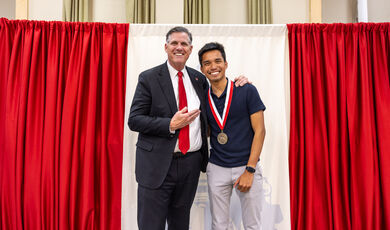 Two men stand together smiling in front of a red curtain