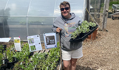 Kristen Nicholson holds several plants in containers at a nursery.