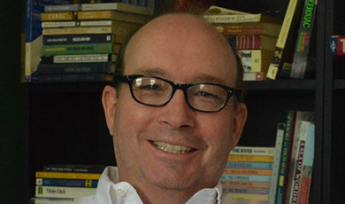 Arthur Lizie smiles in front of a bookshelf.