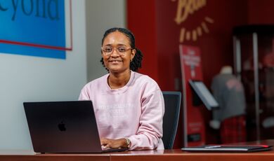 Katia Lopes sits at a table while using a laptop.