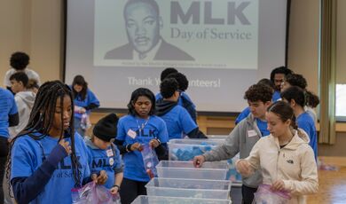 A group of people stand at a table working together in front of a MLK sign