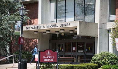 The exterior main entrance to Maxwell Library with a red sign displaying the building's name.