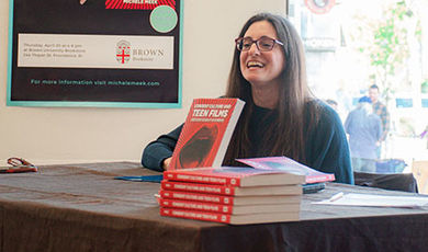 Michele Meek sits at a table with copies of her book on display