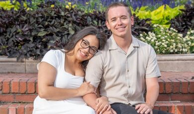 Maddie Monagle and Jonny Matthews sit close together on an outdoor bench,
