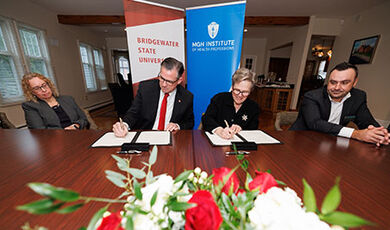BSU and IHP leaders sign an agreement while sitting at a large tables with flowers in front of them.