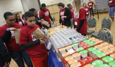 Students and children in red shirts help pack bags of food 