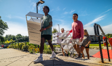 Students holding shelves walk up stairs towards dorms 