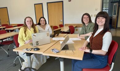 Four people smile while sitting at a table in a classroom.