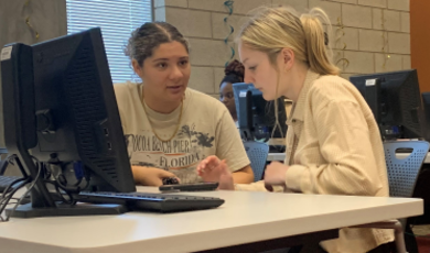 Two women work together in front of a computer screen 