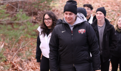 Woman wearing black hat and jacket leads a group of people on path in the woods 