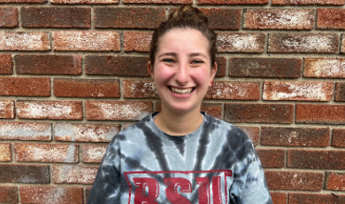 Sara Barry smiles in front of a brick wall 