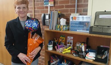 A woman stands holding flowers next to a bookshelf
