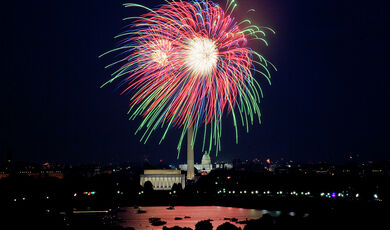 Red and green fireworks burst in the sky over Washington, DC, with the Capitol, Washington Monument, and Lincoln Memorial in view
